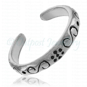 Peut inclure: Une bague d'orteil argent&eacute;e avec un design ouvert. La bague pr&eacute;sente une s&eacute;rie de motifs d&eacute;coratifs noirs en volutes et en points le long de son anneau. La bague est con&ccedil;ue pour &ecirc;tre port&eacute;e &agrave; l'orteil.