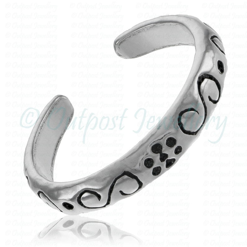 Peut inclure: Une bague d'orteil argent&eacute;e avec un design ouvert. La bague pr&eacute;sente une s&eacute;rie de motifs d&eacute;coratifs noirs en volutes et en points le long de son anneau. La bague est con&ccedil;ue pour &ecirc;tre port&eacute;e &agrave; l'orteil.