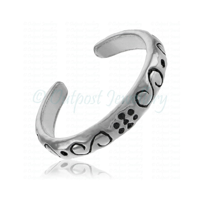 Peut inclure: Une bague d'orteil argent&eacute;e avec un design ouvert. La bague pr&eacute;sente un motif grav&eacute; de volutes et de petits points. Le bijou est con&ccedil;u pour &ecirc;tre r&eacute;glable et est pr&eacute;sent&eacute; sur fond blanc.