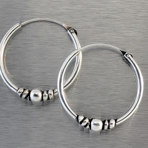 May include: A pair of silver hoop earrings. Each earring features a series of small, round beads clustered together near the bottom. The hoops are circular and have a simple, elegant design, suitable for everyday wear.