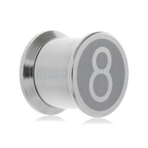 Peut inclure: Un bouchon d'oreille argenté avec une face circulaire affichant le chiffre 8 en blanc sur un disque gris rayé. Le bouchon a un corps cylindrique et une finition métallique polie.
