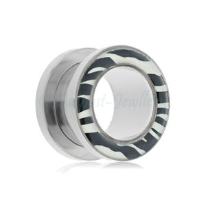 Può includere: Un tunnel per l'orecchio in acciaio inossidabile con un motivo a stampa zebrata in bianco e nero sul bordo. Il tunnel è circolare con un centro cavo, progettato per piercing all'orecchio allungati.