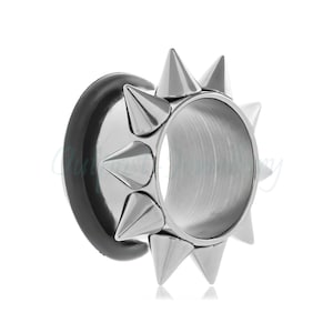 May include: A silver ear gauge with a black curved back and a ring of silver spikes. The gauge is designed to stretch the earlobe. The spikes are evenly spaced around the outer edge of the gauge.