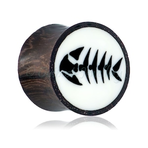 May include: A dark brown wooden ear plug with a white circular face. The face features a black fish skeleton design. The plug is designed to be worn in a stretched ear piercing.