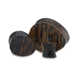 May include: A collection of dark brown wooden ear plugs with a natural wood grain pattern. The plugs are various shapes and sizes, including teardrop and circular designs. Some have a textured surface.