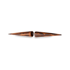 May include: A pair of wooden earrings with a dark brown and black wood grain pattern. The earrings are shaped like elongated cones, connected by a silver-coloured post. The earrings are set against a white background.