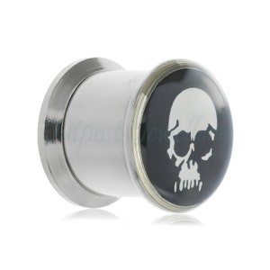 Peut inclure: Écarteur d'oreille blanc et argenté avec une face noire ornée d'un motif de crâne blanc. Le bouchon a une forme cylindrique avec un bord évasé et une finition polie. Un accessoire sur le thème gothique.