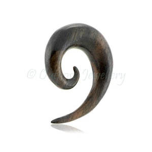 Può includere: Un dilatatore per orecchio a spirale in legno marrone scuro. Il gioiello per il corpo ha una finitura liscia e lucida e un design curvo. Questo gioiello viene utilizzato per allargare i piercing all'orecchio. Misura circa 7 cm di lunghezza.