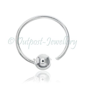 May include: A silver-colored captive bead ring, featuring a small, round bead and a circular design. The ring is made of a shiny, metallic material and is designed for body piercing. The text "Outpost-Jewellery" is visible.