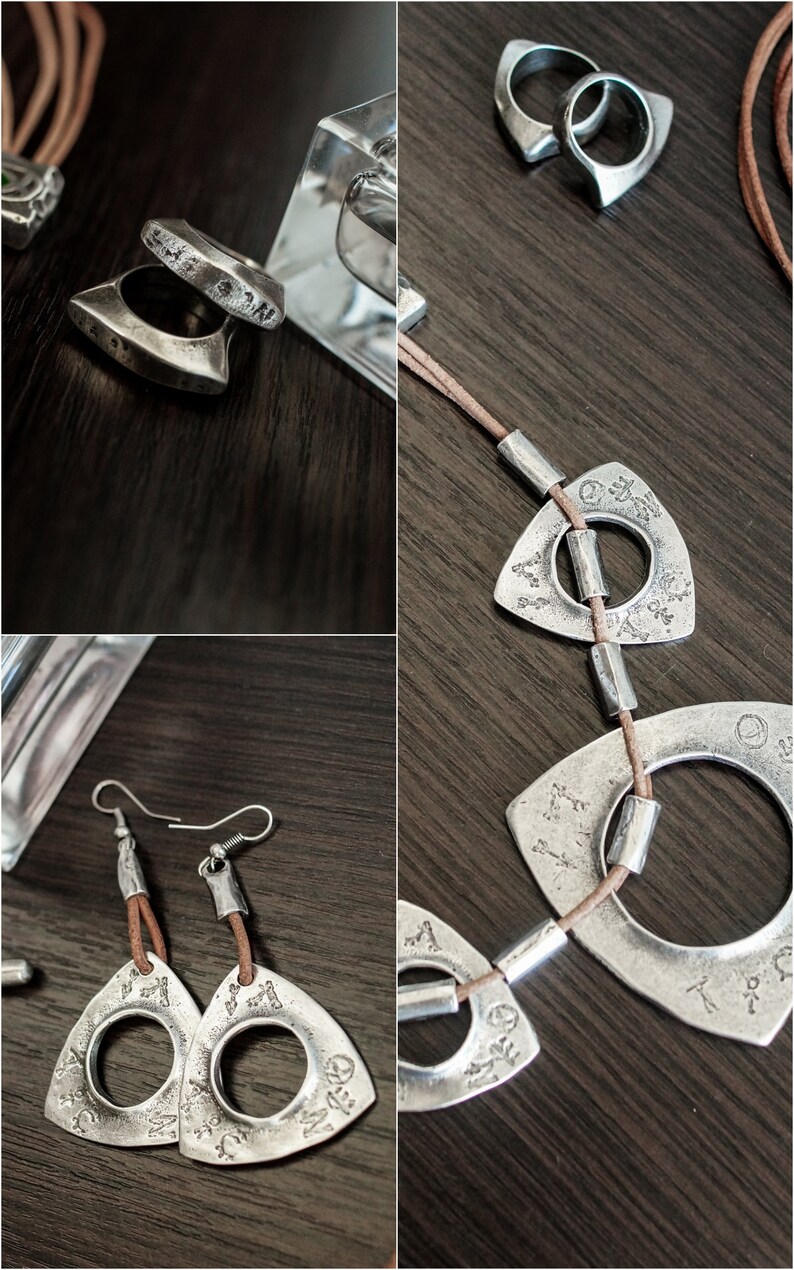 May include: A set of silver jewelry featuring a necklace, earrings, and rings. The necklace has a brown leather cord with silver triangular pendants with circular cutouts. The earrings are similar to the pendants, with a brown leather cord attached to the top. The rings are silver and have a unique, angular design.