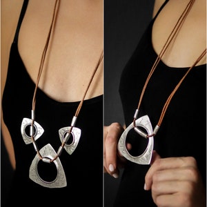 May include: A silver necklace with three triangular pendants, each with a circle cut out. The necklace is made of brown leather cord.