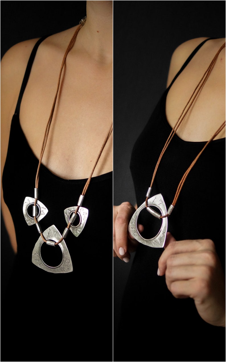 May include: A silver necklace with three triangular pendants, each with a circle cut out. The necklace is made of brown leather cord.