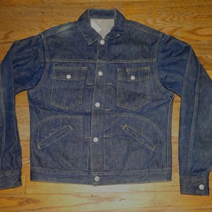 May include: A classic denim jacket in a medium blue wash. It has a button-up front, two chest pockets, and two lower pockets. The long sleeves have buttoned cuffs. The jacket is made of denim. A timeless piece of outerwear.