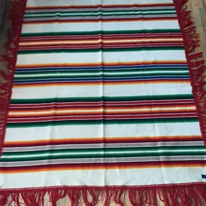 May include: A white blanket with red, green, orange, blue, and yellow stripes. The blanket has a fringe border.