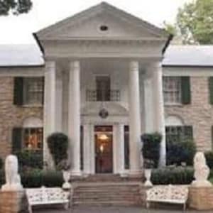 May include: A large, white, two-storey house with a stone facade and a columned porch. The house has a large lawn and a driveway.