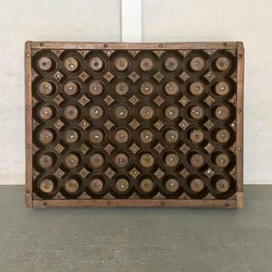 May include: A rectangular wooden tray with numerous circular indentations. The tray is constructed with a dark brown wood frame and features a grid of circular openings, each with a central screw. The tray is designed to hold multiple small items.