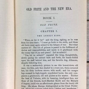 Puede incluir: P&aacute;gina de libro abierto con texto negro sobre papel blanquecino. El t&iacute;tulo es "OLD FRITZ AND THE NEW ERA." El texto contin&uacute;a con "BOOK I. OLD FRITZ. CHAPTER I. THE LONELY KING." El fondo es de madera.