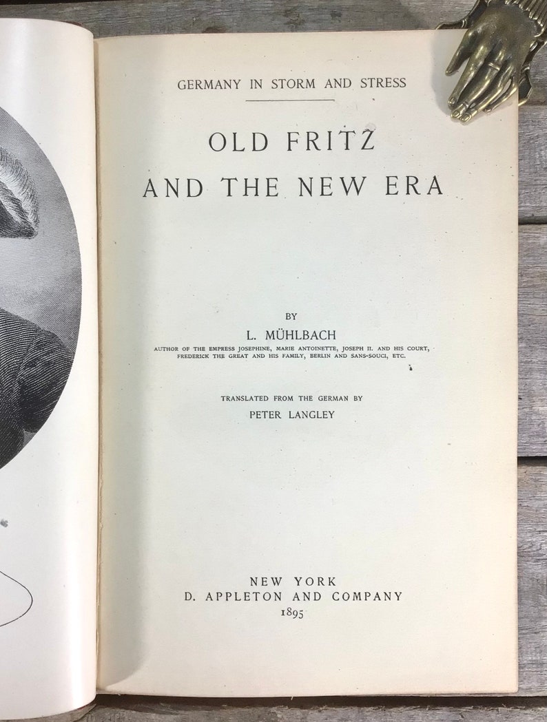 Puede incluir: Libro abierto titulado "Old Fritz and the New Era" de L. M&uuml;hlbach, publicado en 1895 por D. Appleton and Company, Nueva York. El t&iacute;tulo del libro est&aacute; en letras grandes y en negrita. El libro est&aacute; abierto en la portada.