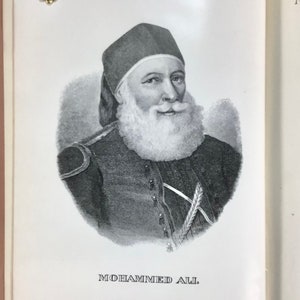 Puede incluir: Un retrato en blanco y negro de Mohammed Ali, de un libro antiguo. El retrato muestra a un hombre con barba blanca y sombrero oscuro. El texto "MOHAMMED ALI" est&aacute; impreso debajo.