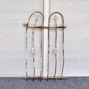 May include: A weathered, rusty metal window grill with an arched top and vertical bars. The design includes decorative fleur-de-lis accents and ornate details. The grill is likely for decorative purposes.