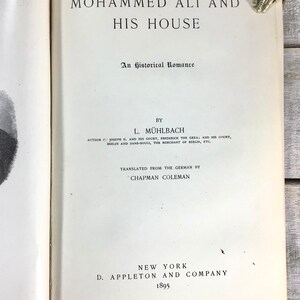 Puede incluir: Libro abierto titulado "Mohammed Ali and His House" con texto negro. El libro es una novela hist&oacute;rica de L. M&uuml;hlbach, traducida del alem&aacute;n por Chapman Coleman, publicada en 1895 por D. Appleton and Company, Nueva York.