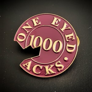 Puede incluir: Un pin de metal granate con letras doradas que dice "One Eyed Jacks 1000".