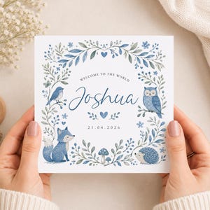 Könnte beinhalten: Eine quadratische weiße Karte mit einer blauen Aquarellillustration eines Waldkranzes mit Vogel, Eule, Fuchs, Igel und Pilzen. Der Text lautet Welcome to the World, Joshua, sowie das Datum 21.04.2026 in einer dunkelblauen Schriftart.