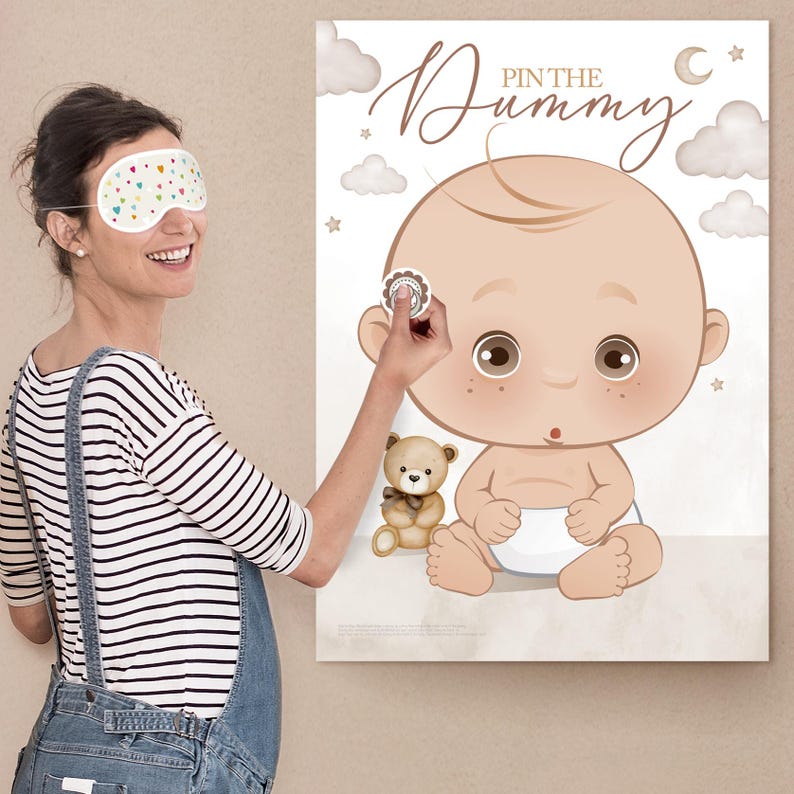 Op de afbeelding: Een babyshower-spel met een grote ge&iuml;llustreerde baby met een luier, een teddybeer en de tekst "Pin the Dummy". Een persoon met een slaapmasker probeert een sticker op de baby te plakken.