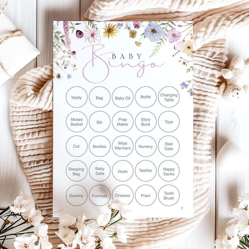 Op de afbeelding: Een Baby Bingo-spelkaart met bloemaccenten in pastelkleuren. De kaart heeft een raster van cirkels met babygerelateerde woorden zoals "Teddy", "Fles" en "Wandelwagen". Het woord "Baby Bingo" staat in een sierlijk lettertype bovenaan.