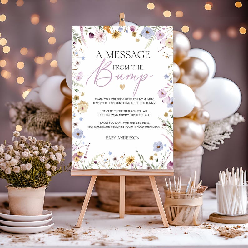K&ouml;nnte beinhalten: Eine Holzstaffelei zeigt ein Schild mit floralen Akzenten und dem Text "A Message From The Bump". Das Schild enth&auml;lt eine Nachricht und den Namen "Baby Anderson". Der Hintergrund zeigt Ballons und dekorative Elemente.