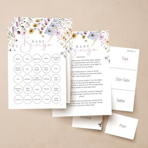 Op de afbeelding: Baby Bingo-spelkaarten met bloemaccenten in paars, blauw en geel. De kaarten bevatten woorden als "Teddy", "Fles" en "Speelgoed". Een aparte kaart leest "Call Card 4" met "Toys" en "Stair Gate".