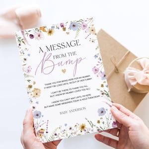 K&ouml;nnte beinhalten: Eine Gru&szlig;karte mit dem Text "A Message From The Bump" in floralem Design. Die Karte enth&auml;lt eine Nachricht vom Baby und den Namen "Baby Anderson". Die Karte wird von einer Person gehalten.