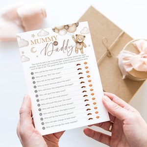 Może przedstawiać: Drukowana karta do gry na baby shower z brązowym misiem trzymającym balony. Karta zawiera tekst "Mummy or Daddy" i listę pytań, na kt&oacute;re goście mają odpowiedzieć o przyszłych rodzicach.