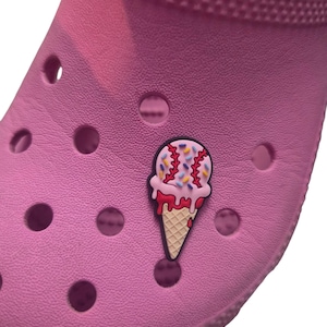 Pode incluir: Um sapato rosa com um adorno de sorvete. O adorno apresenta um cone de waffle com sorvete rosa, gotejamento vermelho e granulado colorido. O sapato tem v&aacute;rios orif&iacute;cios de ventila&ccedil;&atilde;o.