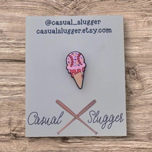 Pode incluir: Um alfinete de sorvete com tema de beisebol com granulado rosa e sorvete vermelho pingando. O alfinete est&aacute; em um cart&atilde;o azul claro com o texto "@casual_slugger casualslugger.etsy.com" e as palavras "Casual Slugger" com bast&otilde;es de beisebol cruzados.