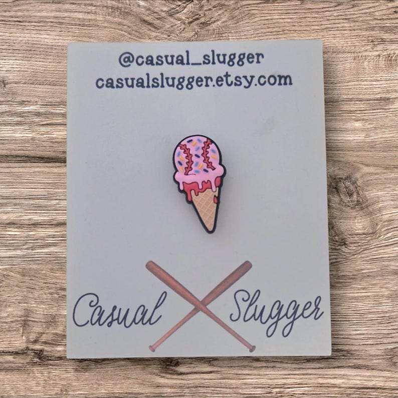 Pode incluir: Um alfinete de sorvete com tema de beisebol com granulado rosa e sorvete vermelho pingando. O alfinete est&aacute; em um cart&atilde;o azul claro com o texto "@casual_slugger casualslugger.etsy.com" e as palavras "Casual Slugger" com bast&otilde;es de beisebol cruzados.