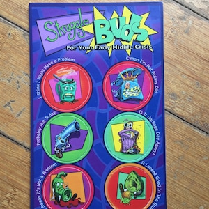 May include: A colorful card with the title "Struggle Buds" and the text "For Your Early Midlife Crisis". The card features five circular images with cartoon characters and humorous phrases, such as "I Think I Might Have a Problem", "Probably Not Today", "C'mon I'm Not Rotary Old", "Is It Garbage Day Again?", and "It Looked Good In The Store".