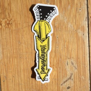 May include: A yellow and black sticker with a zipper design and the text "Kennywood" in a black arrow shape.