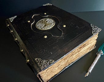 May include: A large, antique-style book with a black leather cover. The cover features ornate metal corner pieces, a central medallion, and brass studs. The aged pages are visible, suggesting a vintage or fantasy theme.
