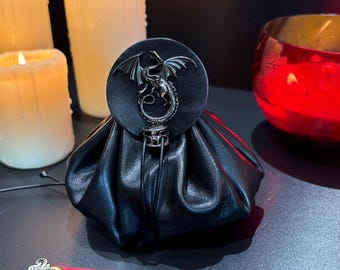 May include: Black leather pouch with a silver dragon emblem on the flap. The pouch is gathered at the top and has a drawstring closure. The background includes lit candles and a red glass bowl.