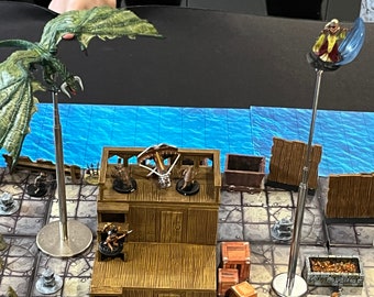 May include: A tabletop game scene with miniature figures, including a green dragon, a figure with a crossbow, and a figure with a blue cape. The figures are on a wooden platform with a blue water background.