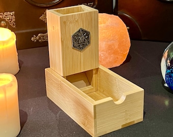 May include: A wooden dice tower with a metal D20 die on the front. The tower has a drawer on the bottom and a slot for dice to fall out of the top.