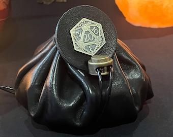 May include: A black leather dice bag with a brass D20 die charm. The bag has a drawstring closure and a brass toggle.
