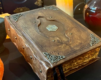 May include: A brown leather-bound journal with ornate metal accents and a decorative metal clasp. The journal has a worn, vintage look and is closed.