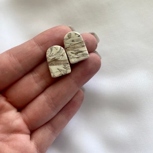 May include: A pair of white and brown marbled ceramic earrings in the shape of an arch.