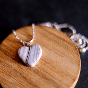 May include: A silver chain necklace with a white and gray heart-shaped pendant. The pendant has a marbled pattern.