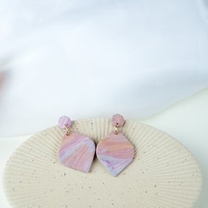 May include: A pair of pink and white marbled teardrop shaped earrings with gold hooks.