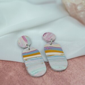 May include: A pair of dangle earrings with a light blue, pink, and yellow marbled design. The earrings are made of polymer clay and have silver hooks.