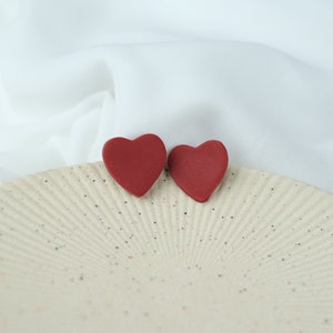 May include: Two red heart-shaped earrings on a white speckled plate.