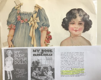 May include: A vintage paper doll book with a cover featuring a girl in a blue dress with a yellow bow. The book is titled "My Book of Paper Dolls" and has a text description about the book's history and different versions. The book is ready to cut out and dress.